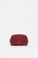 Neceser compacto de nylon color bordó con estructura blanda, cierre superior y logo metálico de la marca en el frente.