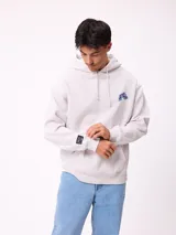 Canguro con capucha y cordones ajustables, de color gris claro. Presenta un logo bordado en el pecho y un parche decorativo en el puño de la manga derecha. Cuenta con un bolsillo frontal tipo canguro y puños acanalados.