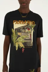Remera Farm Rio de color negro con cuello redondo y mangas cortas. Presenta un estampado frontal con la inscripción de la marca, un tranvía rodeado de vegetación, animales y elementos tropicales.