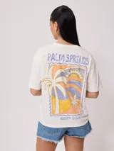 Remera color salmón de corte holgado, con estampado pequeño en el frente que incluye un arcoíris y el texto "Rusty Club".