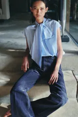 Camisa sin mangas confeccionada en algodón, con cuello redondo y detalle de lazada frontal. Presenta un diseño de corte holgado con bajo redondeado y cierre posterior mediante abertura y botones.