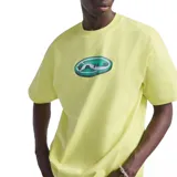 Remera de algodón color amarillo pastel con cuello redondo y mangas cortas. Presenta un estampado gráfico central en forma de óvalo con el logo de la marca en estilo 3D.