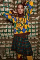 Sweater tejido de algodón con cuello alto marrón, diseño con rombos amarillos, verdes y azules, y bordado frontal de dos figuras.