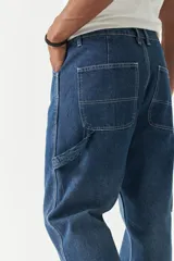 Jean estilo carpenter de corte relajado, recto y amplio, con diseño de cinco bolsillos y costuras reforzadas características del modelo. Presenta un acabado lavado en tono gris oscuro.