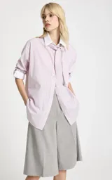 Camisa de algodón con estampado de rayas verticales en tonos rosa y blanco. Presenta cuello clásico, mangas largas con puños anchos en contraste y un detalle de pañuelo integrado en el cuello que simula una corbata. Posee cierre frontal de botones y corte recto.