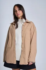 Sobrecamisa color beige confeccionada en gabardina, de corte holgado, con cuello camisero, cierre frontal con botones, dos bolsillos de parche en el pecho y mangas largas con puños abotonados.