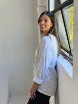 Remera blanca de manga larga con cuello redondo y diseño holgado. Presenta un aplique frontal rectangular con lentejuelas plateadas y detalles de encaje bordado.