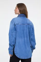Camisa oversize de denim azul claro, con cuello clásico, mangas largas y cierre frontal de broches metálicos.