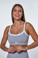 Conjunto deportivo compuesto por un top y un short de tiro alto en color gris. El top presenta breteles blancos, escote redondo y el logo de la marca estampado en el frente. El short cuenta con costuras decorativas blancas que realzan el diseño.