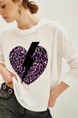 Remera de manga larga color blanco con estampa frontal de un corazón con diseño animal print en tonos violeta y negro, atravesado por un rayo negro.