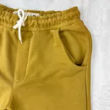 Bermuda deportiva color mostaza, con cintura elástica ajustable con cordón y bolsillos laterales. Presenta un logo pequeño bordado en la pierna derecha.