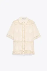 Blusa de algodón color crudo con detalle de bordados y crochet. Cuello redondo, manga corta y cierre frontal con botones.