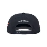 Gorra Supreme de color azul marino, con visera curva y un diseño bordado de calaveras con detalles en rojo alrededor de la corona.