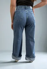 Pantalón de jean azul con efecto lavado, corte wide leg, bolsillos laterales y detalle de botones en el ruedo.