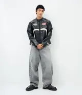 Campera biker de cuero sintético negro con detalles en blanco, cuello mao con broche, cierre frontal y parches bordados en el pecho. Presenta diseño acolchado en los hombros y mangas largas.