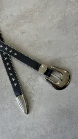 Cinturón negro de cuero sintético con hebilla metálica plateada estilo western y apliques de estrellas plateadas.