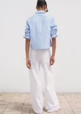 Camisa de corte crop y diseño recto, con estampado de rayas verticales en azul y blanco. Presenta cuello camisero, bolsillo en el pecho, cierre frontal con botones y mangas tres cuartos.