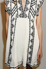 Vestido corto blanco de Zara Woman Collection con bordados en contraste de color negro, escote en V y mangas sisa con pequeños volados.