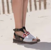 Sandalias de cuero con semi plataforma, talón y tiras en negro charol, y empeine blanco con detalles pintados a mano en rojo. Cuentan con tira ajustable al tobillo con hebilla metálica.