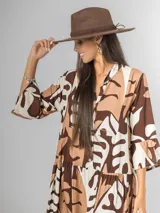 Vestido largo de manga tres cuartos, con cuello camisero y botones frontales. Presenta un estampado abstracto en tonos marrón oscuro, beige y blanco. El calce es amplio y tiene un ruedo con volado.