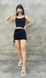 Vestido corto negro ajustado, con breteles finos y detalle de frunce lateral con cordones.