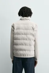 Cazadora acolchada de cuello subido, color negro, con mangas largas de tejido elástico. Incluye bolsillos en la cadera, un bolsillo interior y bajo con elástico. Cierre frontal de cremallera.