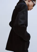 Parka de denim negro de corte largo, con cuello alto, cierre frontal oculto y múltiples bolsillos con solapa en el pecho y los costados. Cuenta con cordón ajustable en la cintura.