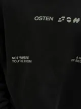 Buzo negro de corte holgado con cuello redondo y puños acanalados. Estampado frontal con la palabra "OSTEN" y la frase "NOT WHERE YOU'RE FROM A MINDSET OF BECOMING" en color blanco.