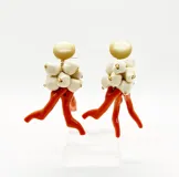 Par de aros colgantes con cabezal beige, cuentas color crudo y piezas tipo coral naranja. Se ajustan con perforación y no contienen níquel.