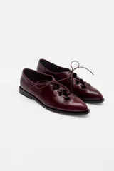 Zapato acordonado de cuero color bordó, con punta fina y diseño estilo oxford. Presenta cordones al tono y detalles de ojales metálicos dorados.