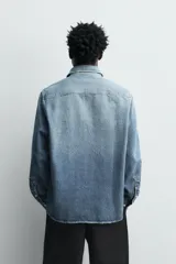 Camisa de corte relajado confeccionada en denim de algodón con efecto lavado. Presenta cuello solapa, cierre frontal de botones y mangas largas con puños abotonados.