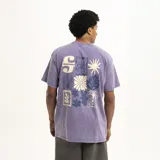 Remera color beige de corte holgado con estampado pequeño en el pecho de una flor y la letra S.