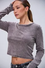 Remera de manga larga color gris con efecto acid wash, cuello redondo y detalles de pedrería plateada alrededor del cuello. Las mangas tienen un diseño que cubre parcialmente las manos.