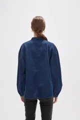 Camisa de jean azul con cuello mao, cierre frontal con botones y mangas largas con puños elásticos fruncidos.
