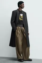 Levita negra de corte relajado confeccionada en tejido con lana. Presenta cuello sin solapa, mangas largas con puños abotonados, bolsillo de vivo en el pecho y bolsillos con solapa en la cadera. Incluye bolsillos interiores, abertura en el centro de la espalda y cierre frontal con botonadura.