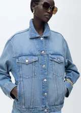 Chaqueta de jean con diseño oversize, cuello camisero, cierre frontal con botones metálicos, dos bolsillos de parche con solapa en el pecho y dos bolsillos laterales de ribete.