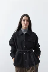 Sobrecamisa de jean color negro con silueta relajada, cuello camisero, cierre frontal con botones metálicos, bolsillos frontales y cinturón ajustable en la cintura.