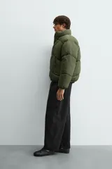Cazadora acolchada tipo puffer de corte relajado, color verde militar. Presenta cuello subido, cierre frontal con cremallera, bolsillos laterales con cierre y puños elásticos.
