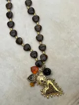 Collar de cuentas de resina en forma de corazón en tonos marrones y ámbar, intercaladas con pequeñas cuentas doradas. Presenta un conjunto de dijes colgantes que incluyen un corazón grande de metal dorado con textura martillada, un dije de corazón sagrado, un corazón pequeño esmaltado y cuentas adicionales en tonos ámbar y negro.