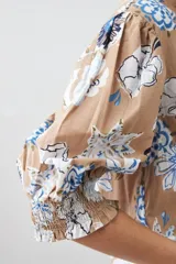 Camisa de manga 3/4 abullonada con puño elastizado, cuello mao y estampado floral en tonos azules y blancos sobre fondo tostado.