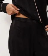 Pijama largo Lov de dos piezas confeccionado en satén negro con rayas sutiles y detalles de vivo en contraste. Consta de una camisa de manga larga con cuello y solapa, abotonado frontal, y un pantalón de calce amplio con cintura elastizada.