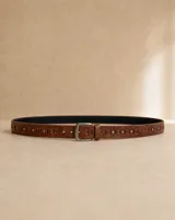 Cinto de cuero sintético marrón claro con detalle de tachas plateadas y presillas decorativas a lo largo de la tira. Cuenta con hebilla metálica rectangular plateada.