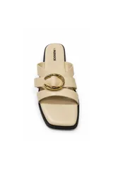 Sandalia plana color beige con punta cuadrada, tiras cruzadas y hebilla metálica dorada decorativa en el empeine.