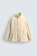 Parka de tejido técnico color beige claro, corte relajado (relaxed fit), con cuello subido, cierre frontal oculto por solapa con botones a presión y bolsillos de solapa en cadera.