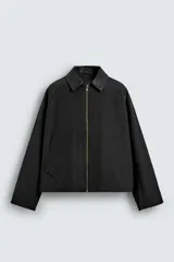 Sobrecamisa de corte relajado en color negro, confeccionada en tejido con algodón. Presenta cuello solapa con efecto piel a tono, cierre frontal con cremallera metálica, bolsillos de vivo en la cadera y mangas largas.
