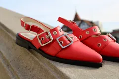 Zapatos tipo mules color rojo con punta cuadrada, dos tiras con hebillas plateadas y detalle de ojalillos metálicos.
