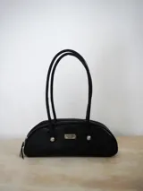 Cartera estilo baguette de cuero con silueta alargada y compacta, diseñada para llevar bajo el brazo. Presenta manijas largas con detalles de nudos esféricos metálicos en las uniones.