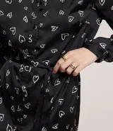 Vestido corto modelo chemise, color negro con estampado de corazones blancos, de manga larga abullonada con hombreras y puños ajustados. Incluye cinturón para lazo en la cintura.