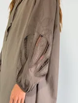 Vestido corto de corte holgado, con cuello camisero y cierre frontal de botones. Presenta mangas tres cuartos con detalles de encaje calado en los laterales y dobladillo asimétrico.