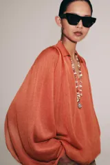 Top de punto color naranja con cuello polo, escote en V y mangas largas amplias con bajo abullonado.
